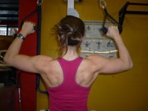 Veronique Rioux wearing pink tank top doing lat pull down with single handles