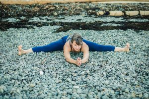 Veronique Roux doing middle split on rocky beach in dark blue legging