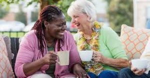 2 women sitting together drinking out of tea cut laughing 